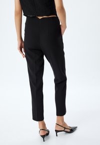 Zwarte op maat gemaakte broek met een aansluitende tailleband, zijzakken en taps toelopende pijpen, gecombineerd met zwarte hakken.