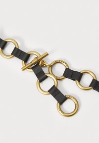 Catena in pelle nera con anelli in metallo color oro e chiusura a morsetto. I dettagli incisi sugli anelli aggiungono accenti notevoli.