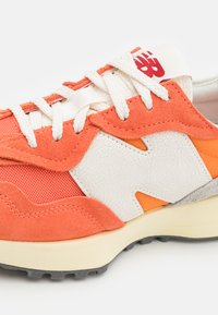 Orange und weiße Sneaker mit Mesh- und Wildledertexturen, ausgestattet mit einem strukturierten weißen Logo, dicker Sohle und kontrastierenden Akzenten.