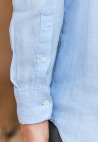 Lichtblauw linnen overhemd met knoopmanchetten, voorzien van een gerelateerde weving, afgeronde manchetranden en vier witte knopen op de mouwen.