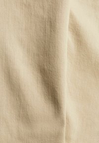 Beżowa tkanina z ukośnym splotem, wykazująca lekkie zmarszczki i miękką teksturę.