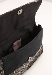 Borsa a mano in tessuto nero con fronte in paillettes, chiusura a pressione magnetica e tasca interna. Texture morbida, forma rettangolare e etichetta di marca all'interno.