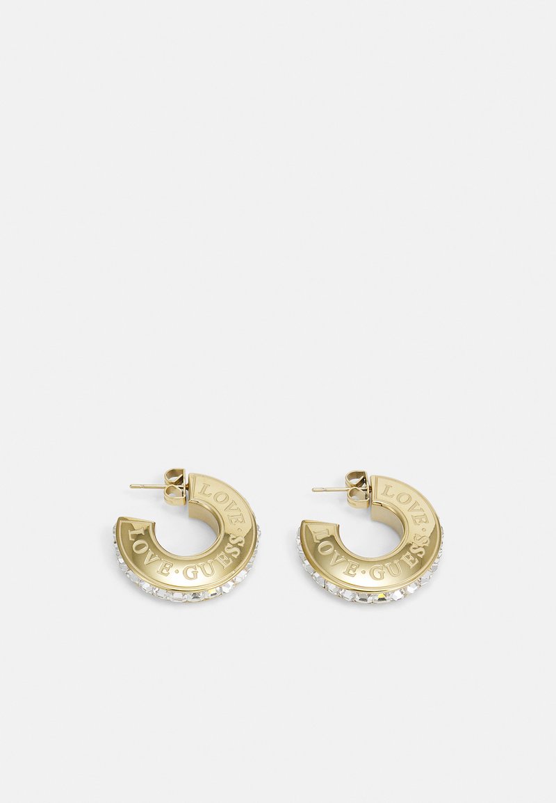 Guld hoop øreringe prydet med "LOVE GUESS" og dekoreret med klare krystaller langs den ydre kant, præsenteret på en hvid baggrund.