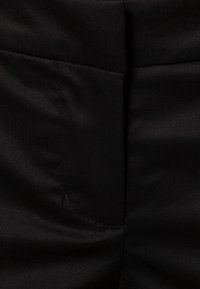 Černá látka s hladkým povrchem, s detailem kapsy na levé straně a jemným leskem. Jednoduchý, elegantní design vhodný pro různé styly.