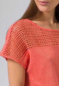 Korallfärgad t-shirt med en texturerad spetsok. Kort ärm, avslappnad passform och slätt material med en lätt melerad look.