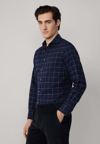 Camicia quadrata blu navy con colletto button-down, maniche lunghe e leggere rifiniture dorate nel motivo tartan. Tessuto morbido.