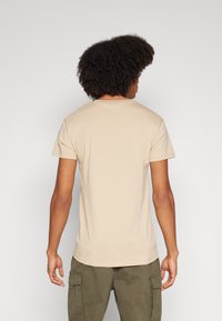 Beige katoenen t-shirt met korte mouwen, een ronde hals en een ontspannen pasvorm, gezien vanuit de achterkant. Draagt een olijfgroene cargobroek.