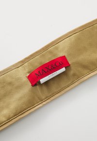 Zlatni satenski materijal s glatkom teksturom, koji sadrži istaknutu crvenu etiketу s natpisom "MAX&Co." i oznaku pričvršćenu bijelom nitom.