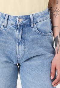 Jeans taille haute en denim bleu clair avec une finition délavée, dotés d'une fermeture à bouton, de passants de ceinture et de poches latérales. Tissu texturé, coupe droite.