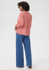 Cămașă corai cu guler și mâneci lungi, având manșete texturate. Asortată cu pantaloni din denim albastru cu picioare largi, care oferă o potrivire lejeră.