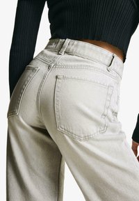 Ljusbeige högmidjade jeans med rak passform, som har två bakfickor och en subtilt strukturerad tyg. Midjan är åtsittande.