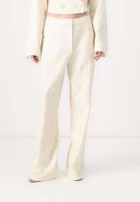 Cream-colored, tailored pants with a slightly flared leg, featuring a textured floral pattern and a smooth fabric finish.