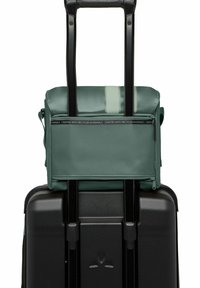 Valigia nera su ruote con una borsa superiore verde a zip staccabile, caratterizzata da una superficie liscia e una striscia decorativa, realizzata con materiali riciclati.