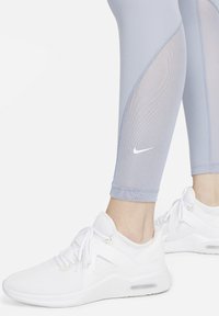 Leggings azzurri chiari con pannelli in rete e un piccolo logo Nike bianco, abbinati a scarpe da ginnastica bianche con un design testurizzato e lacci.