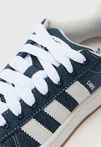 Zapatillas de lona en azul oscuro con cordones blancos, con tres franjas blancas y sutiles detalles de textura en la parte superior. Suela de goma.