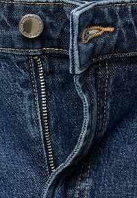 Jeans i denim med en mörkblå tvätt, med en silverknapp och dragkedja. Exponerade sömmar och kontrasterande guldfärgad sömnadsdetalj.