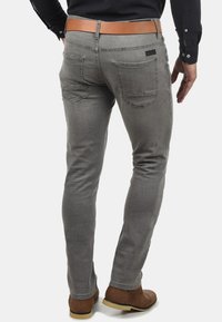 Grå slim-fit jeans med baklommer, subtile sømdetaljer, og et belte i lys skinn. Glatt tekstur og moderne design.