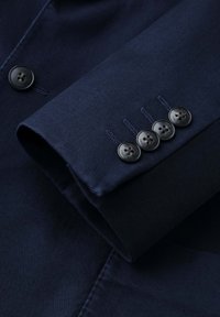 Ärmel eines marineblauen Blazers mit vier schwarzen Knöpfen neben jeder Manschette genäht und einem sichtbaren Knopf am Körper des Blazers.