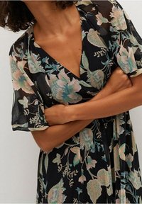 Robe noire  à fleurs avec un tissu transparent, dotée de manches amples et d'un décolleté en V. Le motif comprend des fleurs et des feuilles colorées.