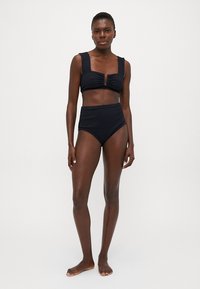 Fekete bikini szett, amely egy kulcslyuk részlettel és széles pántokkal ellátott cropped toppot, valamint magas derekú alsót tartalmaz a megfelelő takarás érdekében.
