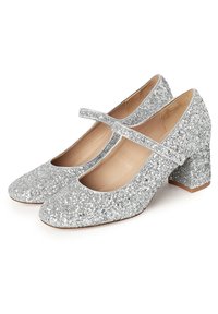 Zapatos tipo Mary Jane en glitter plateado con punta redondeada, correa ajustable y tacón ancho. Forro interior suave con exterior texturizado y brillante.