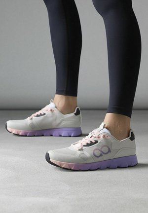 Zapatillas deportivas de color gris claro con una suela morada, detalles en cordones rosas y un diseño de malla con un logotipo cerca del tobillo. Suela exterior de goma texturizada.