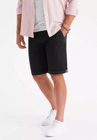 Shorts noirs avec des poignets retroussés, fabriqués en tissu robuste. Associés à une chemise rayée rose et des baskets blanches. Design minimaliste sans motifs.