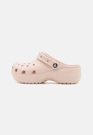 Beige instapslof met ventilatiegaten, een gestructureerde zool en een verstelbare achterriem met een kleine logoknop.