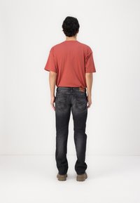 Röd kortärmad t-shirt med avslappnad passform, i kombination med mörkgrå jeans med en diskret tvätt, rak skärning och bakfickor med sömnadsdetaljer.