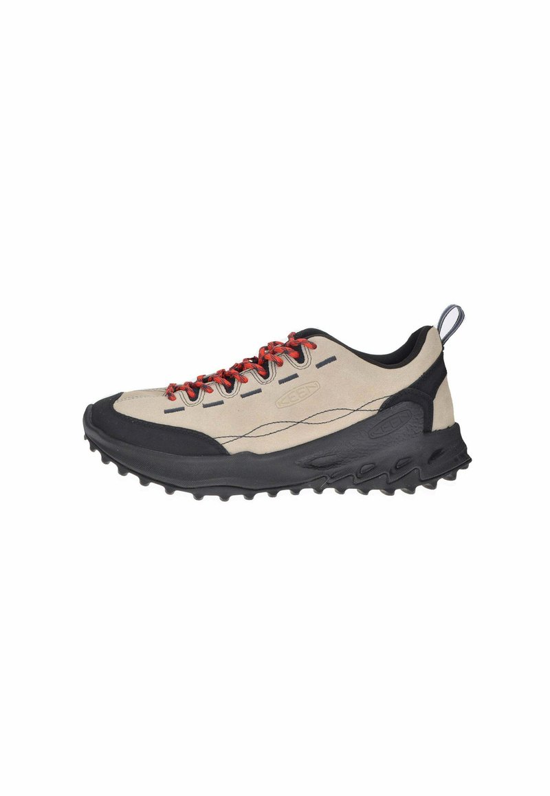 Scarpa sportiva beige chiaro e nera con lacci rossi, suola in gomma testurizzata e puntale rinforzato. Parte superiore in materiale sintetico con dettagli cuciti.