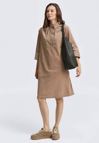 Brun skjortekjole i hør med krave, 3/4-lange ærmer, knapdetalje foran, stylet med beige sneakers og en sort tote-taske.