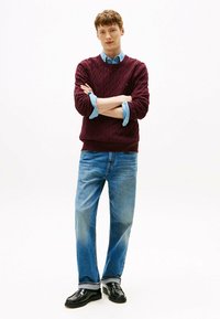 Burgundy cable-knit sweater, denim shirt underneath, paired with light blue straight-leg jeans and black loafers. Simple, textured design.