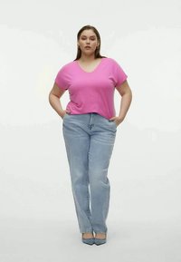 Rosa v-ringad t-shirt med avslappnad passform, kombinerad med ljusblå raka jeans. Modellen står med händerna i fickorna och bär blå klackar.