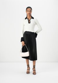 Ribbed white sweater with black collar, black pleated skirt, pink handbag, and black strappy heels. The outfit combines contrast in color and texture.