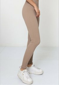 Leggings beiges à côtes avec une taille haute. Associés à des baskets blanches à plateforme dotées d'une semelle texturée et d'un laçage.