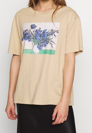 Beżowy t-shirt z krótkim rękawem z nadrukiem przedstawiającym biały wazon z niebieskimi kwiatami na zielonej powierzchni.