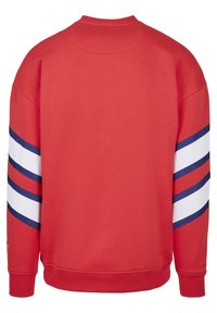 Roter Pullover mit Rundhalsausschnitt, ausgestattet mit weißen und blauen Streifen an den Ärmeln. Hergestellt aus einem weichen, strukturierten Material. Gerippte Bündchen und Saum.