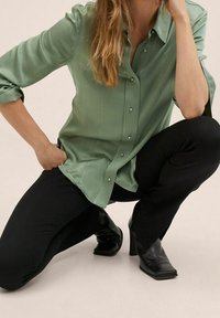 Camicia verde chiaro a maniche lunghe con texture liscia, abbinata a pantaloni neri fitted e stivali neri alla caviglia con punta.