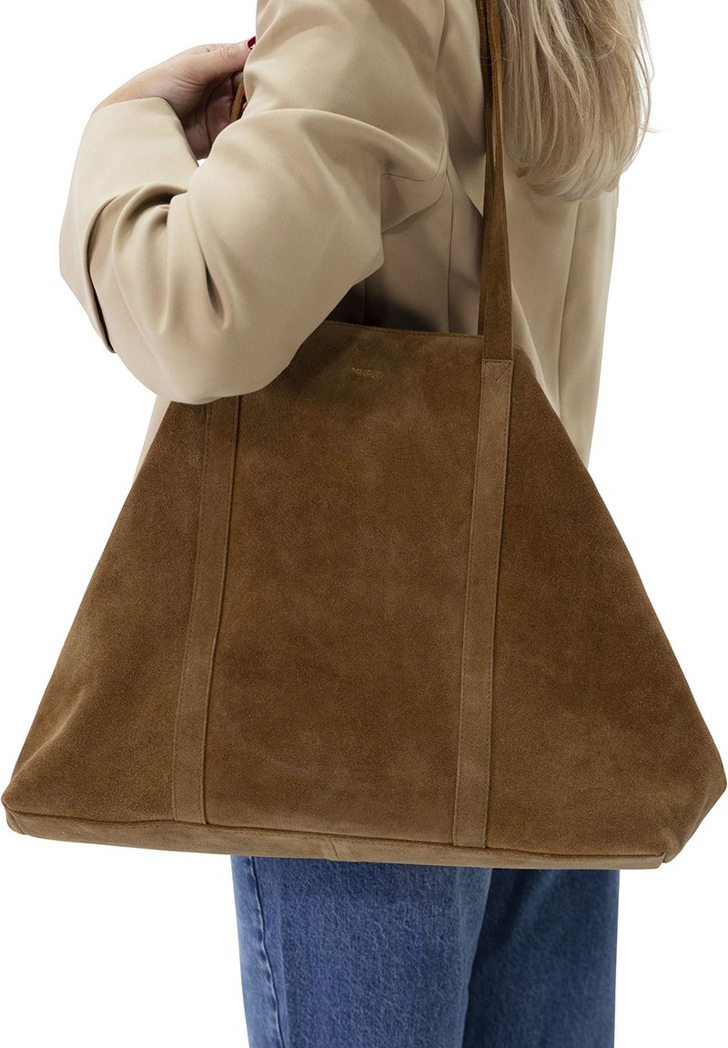 Braune Wildleder-Tote mit weicher Textur, kantiger Form und langen Griffen. Verfügt über vertikale Nähte und ein dezentes Logo auf der Vorderseite.