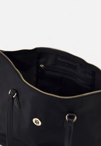 Czarna nylonowa torba typu tote z zamkiem błyskawicznym, złotymi okuciami, wewnętrzną kieszenią na zamek oraz podwójnymi skórzanymi paskami na ramię.