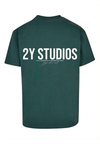 Zelené bavlněné tričko s výrazným bílým textem na zadní straně: "2Y STUDIOS" a "POUZE PRO ČLENY KOMUNITY." Klasický střih, krátké rukávy.