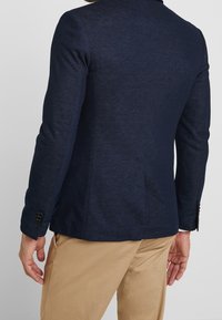 Marinblå blazer i strukturerat tyg, skräddarsydd passform och enkelknappade manschetter. Har ventilerad rygg och minimalistiska design detaljer.