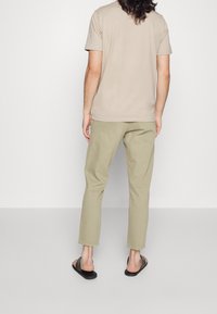 T-shirt in cotone beige abbinata a pantaloni in cotone khaki, caratterizzati da una vestibilità comoda e completata da sandali neri senza lacci. Design semplice, senza fantasie.