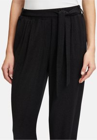 Zwarte, hoge taille broek van een textuurstof. Beschikt over een brede strikriem in de taille en een geplooid voorontwerp.