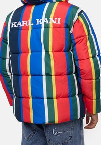 Giacca imbottita con audaci righe verticali in rosso, blu, verde e giallo. "KARL KANI" ricamato sul retro, con una texture liscia.