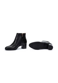 Bottines en cuir noir avec une finition lisse, design asymétrique, fermeture éclair sur le côté et un talon bloc de hauteur moyenne. Semelle en caoutchouc texturé.