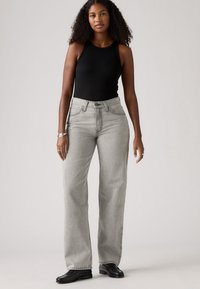 Grijze high-waisted jeans met een rechte pijp, vijfzakkenstijl en contrasterende stiksels, gecombineerd met een zwart mouwloos topje en zwarte schoenen.