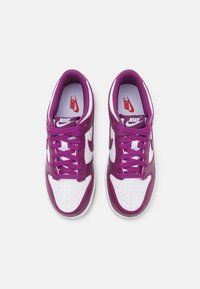Baskets Nike blanches et violettes avec une tige en cuir lisse, un col rembourré et une semelle en caoutchouc. Les caractéristiques incluent un bout perforé et des lacets contrastants.