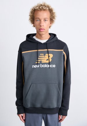 Sudadera con capucha en gris oscuro con acentos en gris claro, que presenta un bolsillo frontal y un gran logo de New Balance en amarillo y blanco.