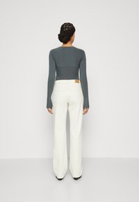Top ajustado de manga larga en gris oscuro combinado con jeans blancos de pierna ancha. Los detalles notables incluyen una etiqueta en la cinturilla y mangas texturizadas.